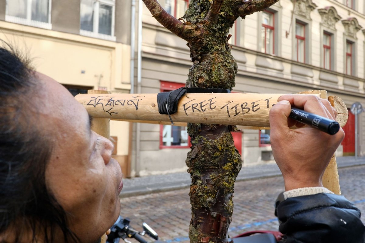 Chungpo Tsering píše „Free Tibet" na dřevěný sloup